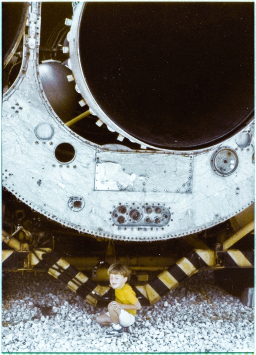 Kai MacLaren pauses to rest for a moment in the shade of the Booster Engine of the Atlas ICBM supported on its transport semitrailer, which was on display at the Air Force Space and Missile Museum at Cape Canaveral Air Force Station, Florida. To the left of the large round dark opening of the Booster Engine nozzle, a bit of one of the spherical tanks which held pressurized gas used to for fuel and oxidizer tank pressurization as well as a variety of other systems which required pressurized gas to function, can be seen, and in the darkness beyond that, a bit of the turbomachinery which powered the engine can also be seen. Photograph by James MacLaren. Kai MacLaren pauses to rest for a moment in the shade of the Booster Engine of the Atlas ICBM supported on its transport semitrailer, which was on display at the Air Force Space and Missile Museum at Cape Canaveral Air Force Station, Florida. To the left of the large round dark opening of the Booster Engine nozzle, a bit of one of the spherical tanks which held pressurized gas used to for fuel and oxidizer tank pressurization as well as a variety of other systems which required pressurized gas to function, can be seen, and in the darkness beyond that, a bit of the turbomachinery which powered the engine can also be seen. Photograph by James MacLaren.